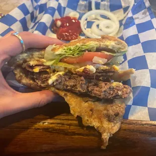 a hand holding a large hamburger