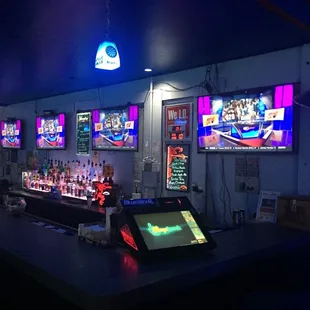 a bar with multiple televisions and neon lights