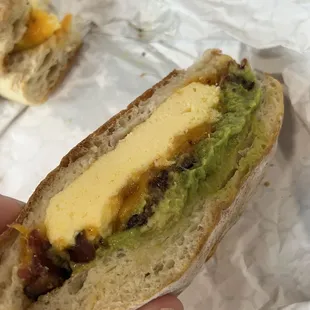 a hand holding a sandwich with cheese and guacamole