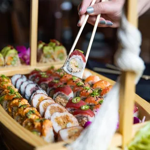 a person holding chopsticks over a boat of sushi