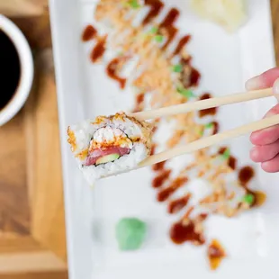 a person holding chopsticks over a plate of sushi