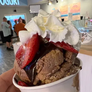 a hand holding a cup of ice cream and strawberries