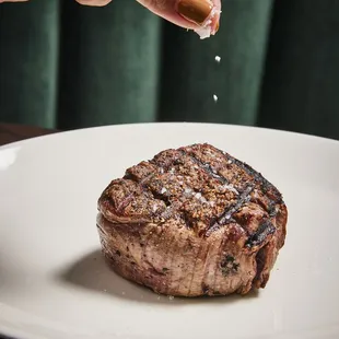 a hand sprinkling salt onto a piece of steak