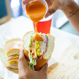 a person pouring sauce onto a sandwich