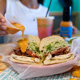 a person pouring sauce on a sandwich