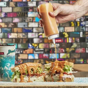a person pouring ketchup on a sandwich
