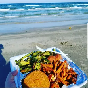 a person holding a plate of food on the beach