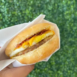 a hand holding a sausage and egg sandwich