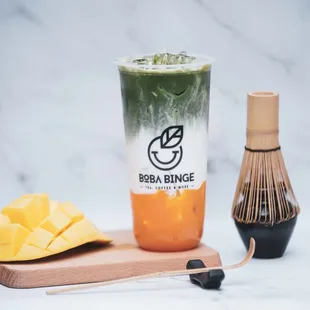 a glass of boba binge next to a whisk of mango and a whisk