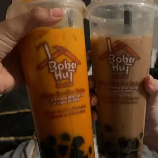 a person holding two cups of boba hut