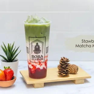 a glass of matcha milk tea next to a bowl of strawberries