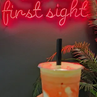 a person holding a drink in front of a neon sign