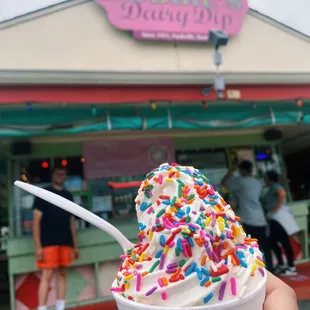a hand holding a cup of ice cream with sprinkles