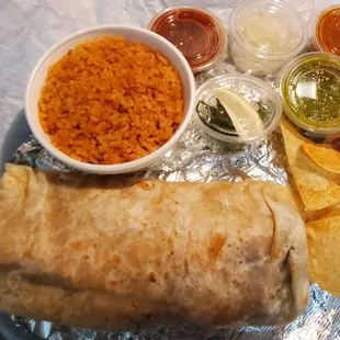 Take-out order of Monster Burrito, chips, side of rice, and containers of salsas and toppings from the salsa bar.