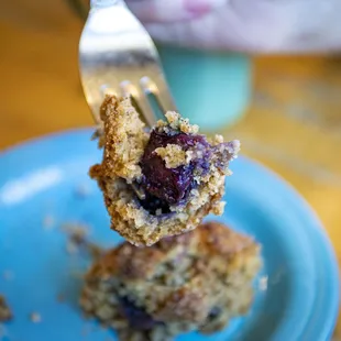 a fork taking a bite of a blueberry muffin