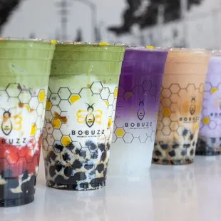 a row of different drinks in plastic cups