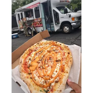 a person holding a pizza in front of a food truck