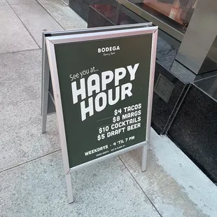a happy hour sign on a sidewalk