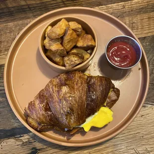 a croissant sandwich and potatoes on a plate
