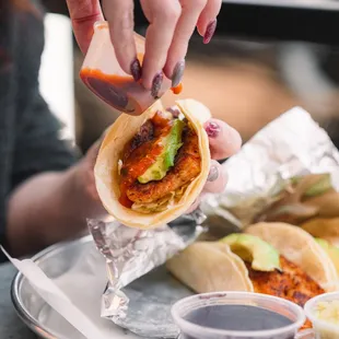 a woman putting sauce on a taco