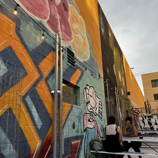 two people sitting on a bench in front of a colorful mural