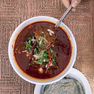 a person holding a spoon over a bowl of soup