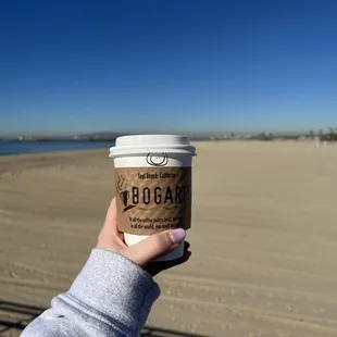 a person holding a cup of coffee on the beach