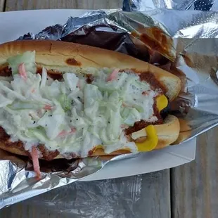 Grilled hotdog with sauces, mustard, and slaw.