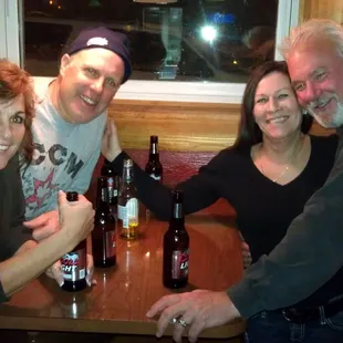 three people sitting at a table with beer bottles
