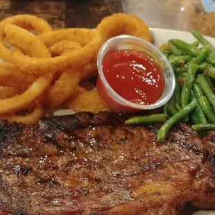 Well-done ribeye steak with green beans and onion rings.