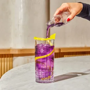a purple drink being poured into a tall glass