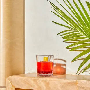a glass of red drink and a palm leaf