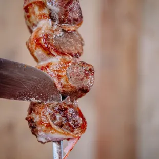 a person cutting meat on a skewer