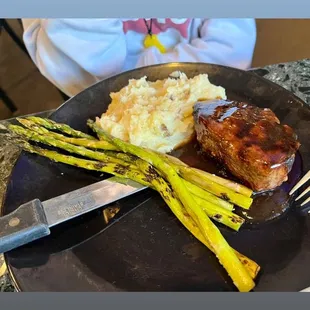 a plate of food with meat, mashed potatoes and asparagus