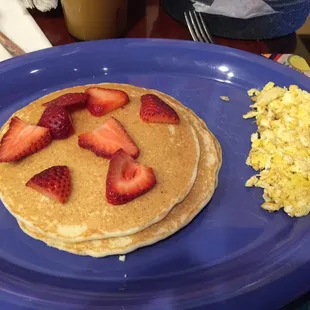 3 pancakes topped with strawberries and one scrambled egg.