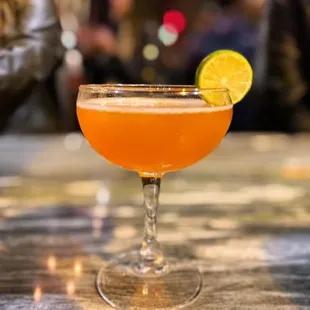 a cocktail in a coupe glass with a slice of lime on the rim