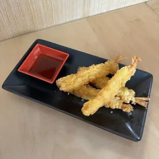  a black plate with fried shrimp sticks and dipping sauce