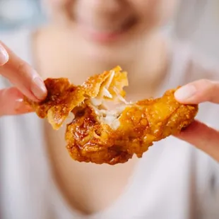 a woman holding a piece of fried chicken