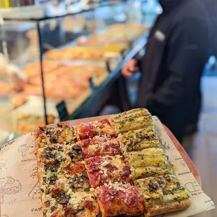 a person holding a pizza in front of a counter