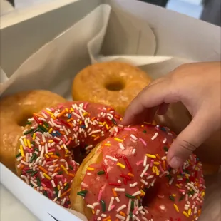 a hand picking a donut from a box