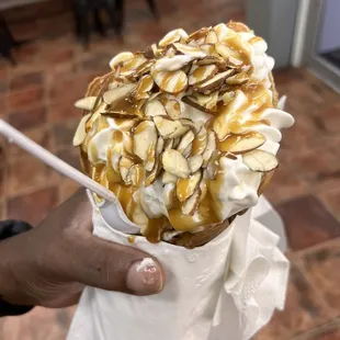 Vanilla ice cream with almonds, whipped cream, caramel and strawberries inside of a bubble waffle cone
