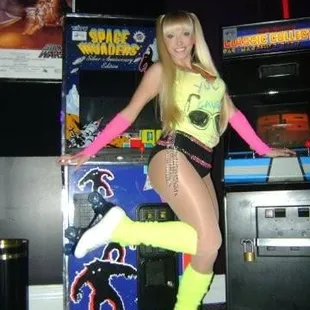a woman in a neon outfit posing in front of a pinball machine