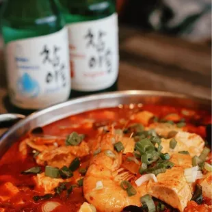 a bowl of seafood stew with a bottle of beer in the background
