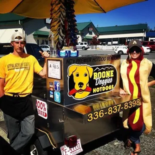 a man and a woman standing next to a hot dog cart