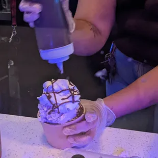 a person pouring chocolate syrup into a bowl of ice cream