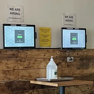 a table with a bottle of water and two monitors on the wall