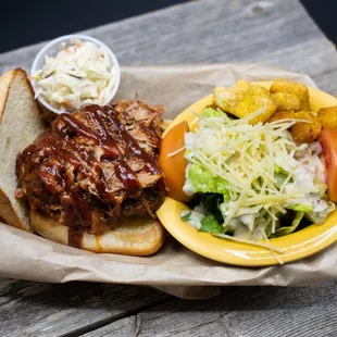 a pulled pork sandwich with cole slaw and a side salad
