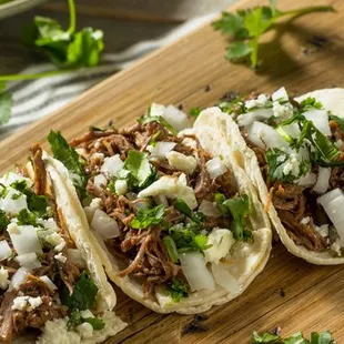 three beef tacos on a wooden cutting board