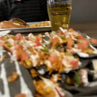 Blurry chicken nachos and cider with cheeseburger and fries in the distance.