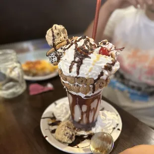 a chocolate milkshake with whipped cream, ice cream, chocolate sauce, and sprinkles